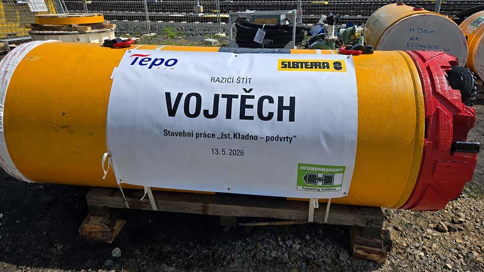 Large yellow tunneling shield component on a wooden pallet at a construction site, with a white banner reading VOJTECH, Razic&iacute; &scaron;t&iacute;t, date 13.5.2026, and logos from Tepo, Subterra, and Herrenknecht.