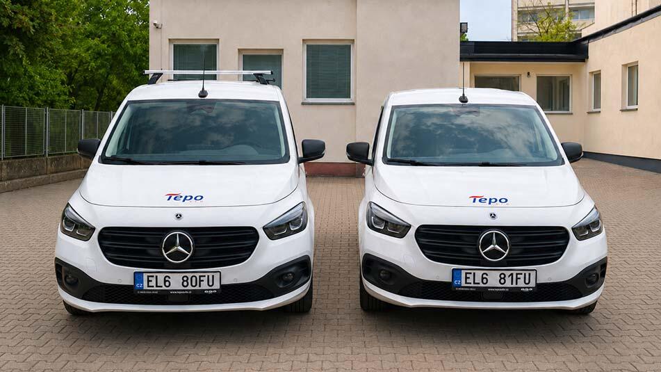 Two white Mercedes vans parked side by side on a paved driveway in front of a beige building, with Tepo logos on the hoods.