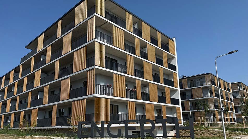 Modern four-story apartment building with vertical wooden slats, white balconies, and a clear blue sky.